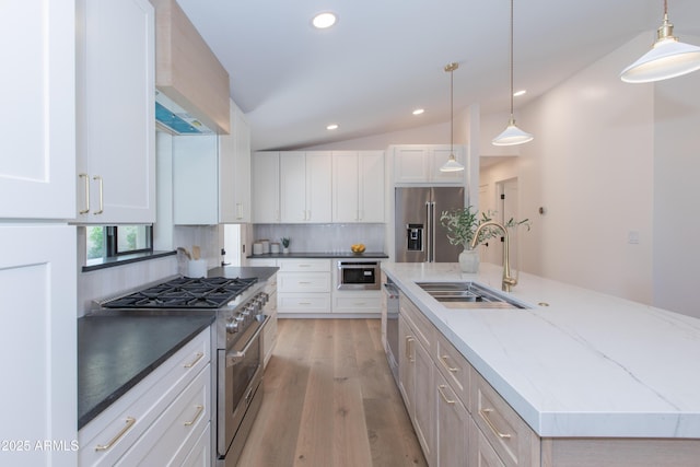 kitchen with high quality appliances, a sink, backsplash, a center island with sink, and light wood-style floors