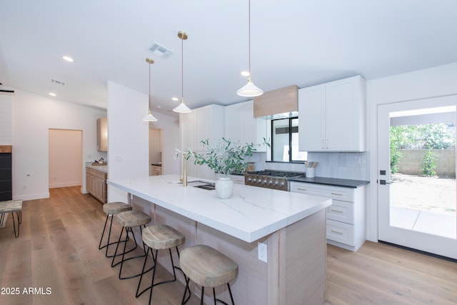 kitchen with a sink, light wood-type flooring, a breakfast bar area, white cabinets, and recessed lighting