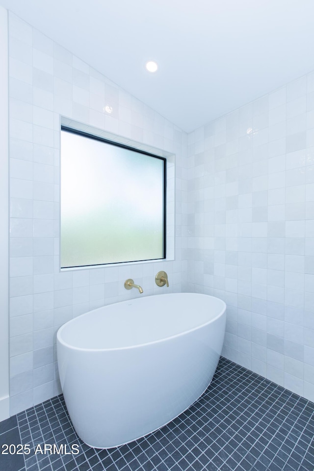 bathroom with tile walls, tile patterned flooring, and a freestanding tub