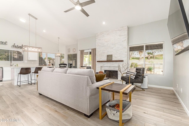 living room with a fireplace, high vaulted ceiling, a healthy amount of sunlight, and light wood-type flooring