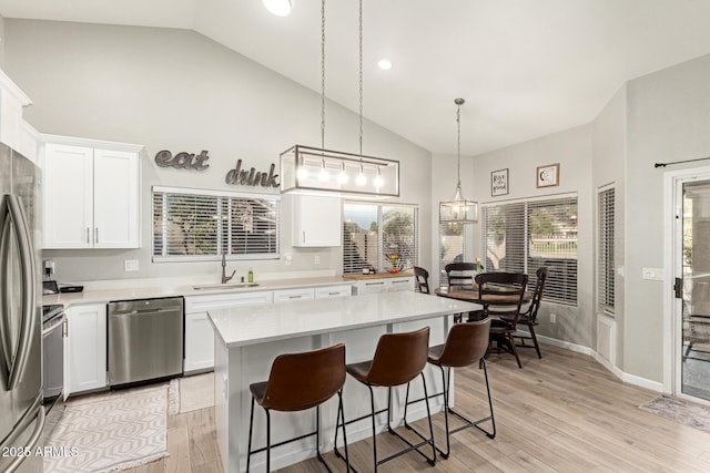 kitchen with pendant lighting, sink, appliances with stainless steel finishes, white cabinets, and a kitchen island