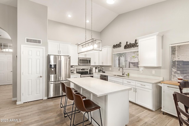 kitchen featuring sink, decorative light fixtures, a center island, stainless steel appliances, and white cabinets