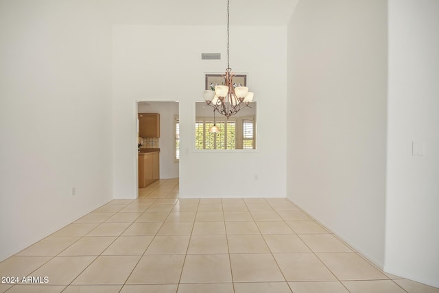 tiled spare room featuring a towering ceiling and an inviting chandelier