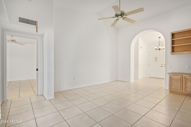 tiled spare room with ceiling fan with notable chandelier, built in features, and high vaulted ceiling