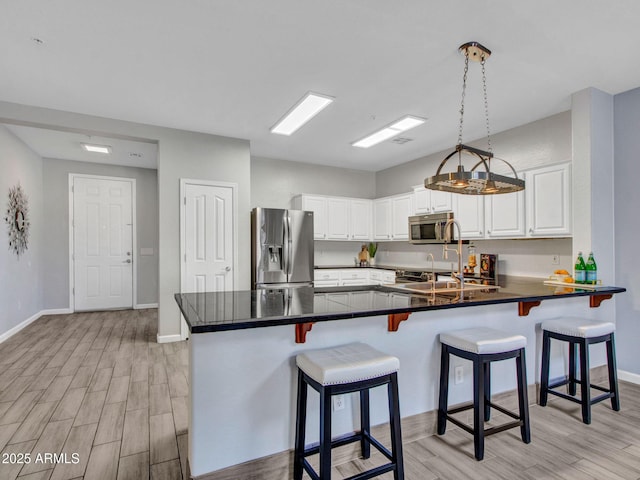 kitchen with pendant lighting, appliances with stainless steel finishes, white cabinetry, a kitchen breakfast bar, and kitchen peninsula