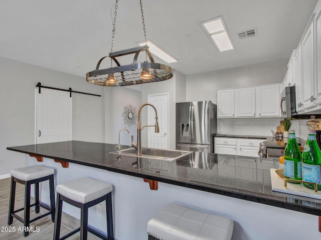 kitchen with white cabinetry, sink, a breakfast bar area, stainless steel appliances, and a barn door