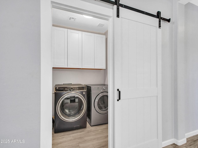 laundry room with cabinets, a barn door, separate washer and dryer, and light wood-type flooring