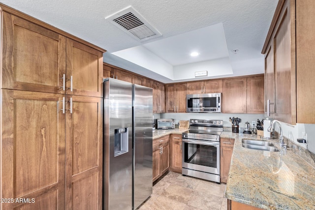 kitchen featuring appliances with stainless steel finishes, sink, a tray ceiling, light stone countertops, and a textured ceiling