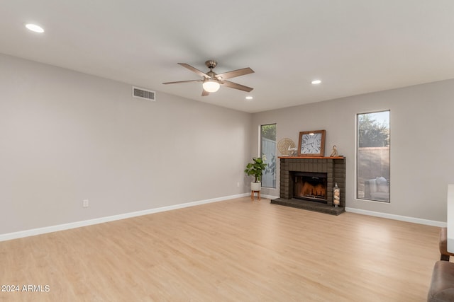 unfurnished living room with a brick fireplace, light wood-type flooring, and ceiling fan