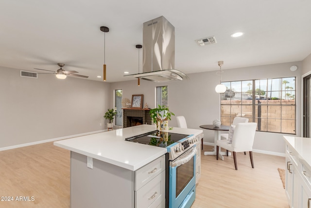 kitchen featuring island exhaust hood, stainless steel range with electric stovetop, a brick fireplace, pendant lighting, and white cabinets