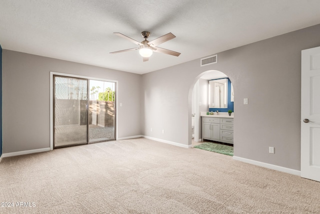 unfurnished bedroom with light carpet, a textured ceiling, ensuite bath, and ceiling fan