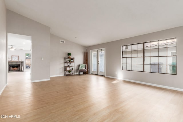 spare room featuring lofted ceiling, a fireplace, light wood-type flooring, and ceiling fan