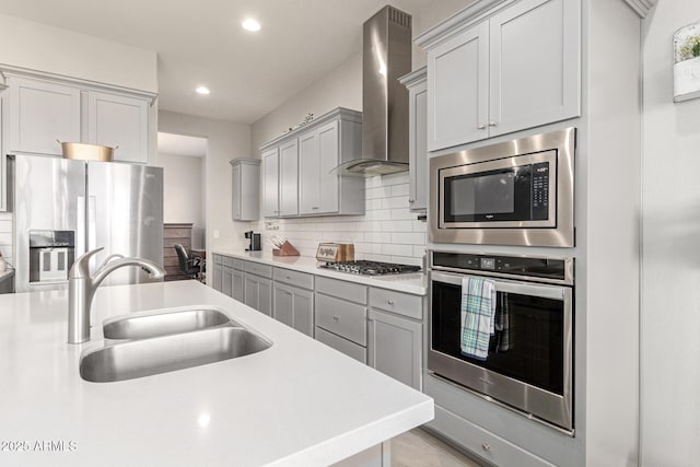 kitchen with wall chimney exhaust hood, sink, appliances with stainless steel finishes, gray cabinets, and decorative backsplash