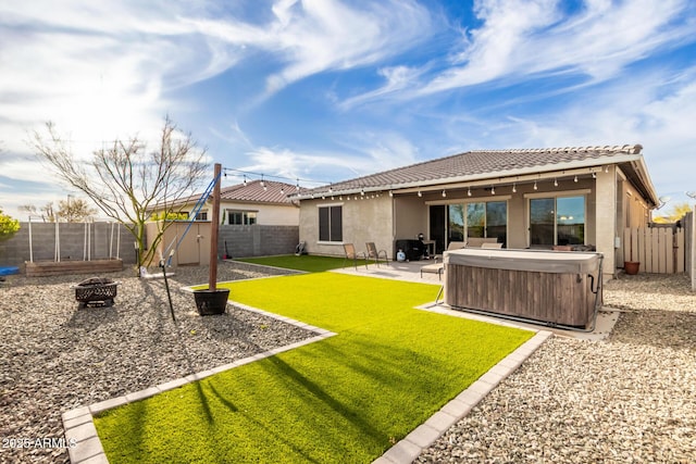 rear view of property with a hot tub, an outdoor fire pit, a patio area, and a lawn