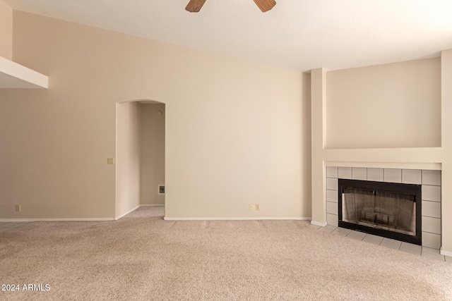 unfurnished living room with ceiling fan, light colored carpet, and a tiled fireplace