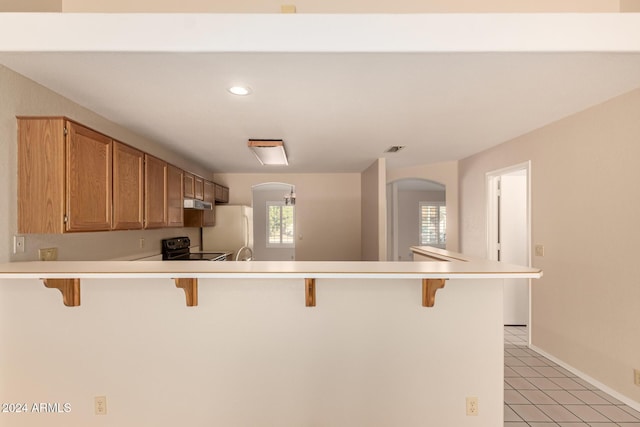 kitchen featuring a breakfast bar, white fridge, kitchen peninsula, and black range with electric cooktop