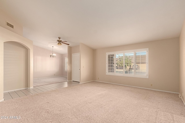 carpeted spare room with ceiling fan with notable chandelier and lofted ceiling