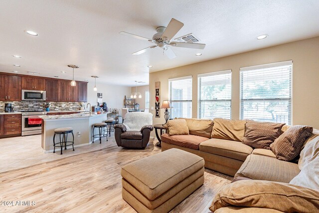 living room with light wood-type flooring, ceiling fan with notable chandelier, and sink