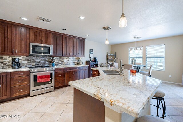 kitchen featuring sink, a kitchen island with sink, backsplash, and stainless steel appliances