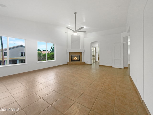 unfurnished living room with light tile floors, ceiling fan, and a towering ceiling