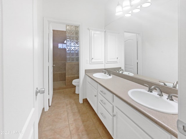 bathroom featuring tile flooring, toilet, tiled shower, double sink, and large vanity