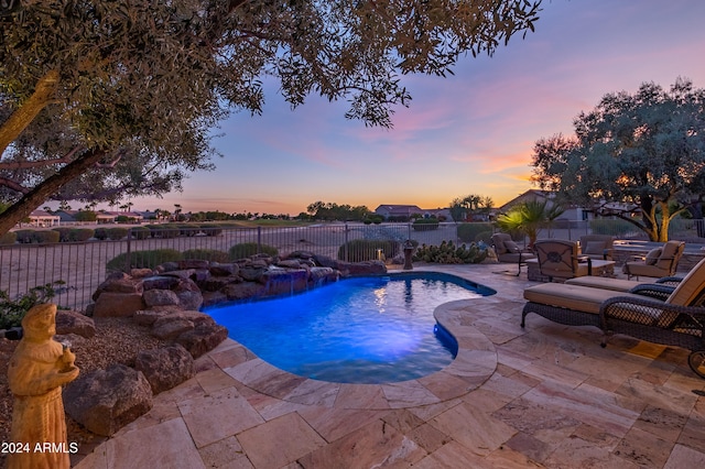 pool at dusk featuring pool water feature, a patio, and a fire pit