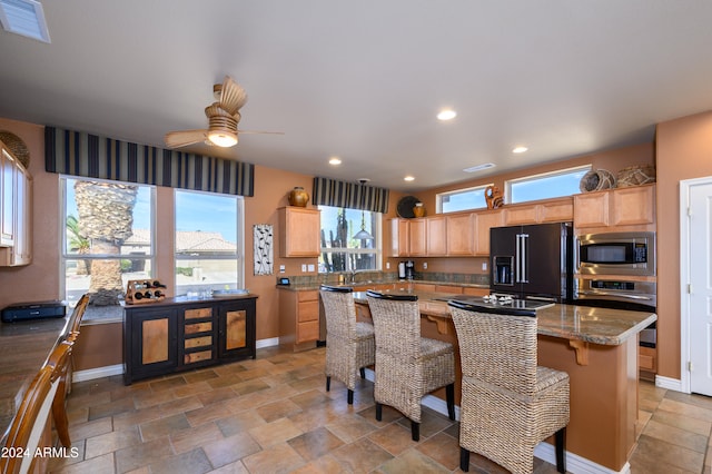 kitchen featuring a center island, light brown cabinets, ceiling fan, dark stone countertops, and appliances with stainless steel finishes