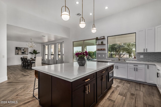 kitchen with a kitchen island, pendant lighting, tasteful backsplash, white cabinets, and dark brown cabinets