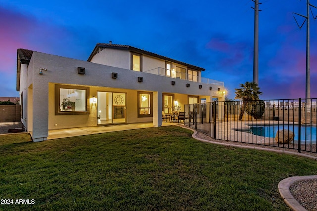 back house at dusk featuring a fenced in pool, a lawn, a patio, and a balcony