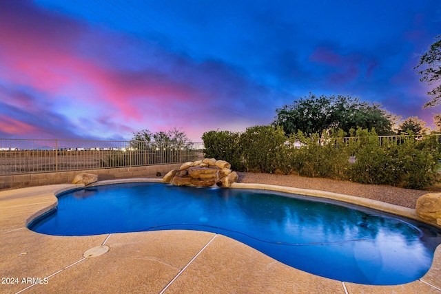 pool at dusk with pool water feature and a patio