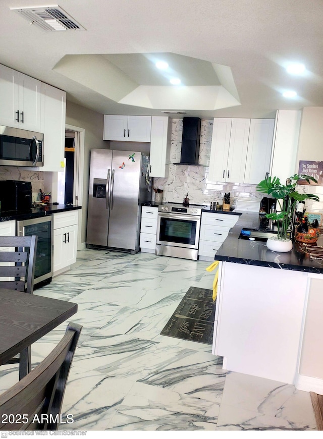 kitchen featuring stainless steel appliances, wall chimney range hood, white cabinets, and decorative backsplash