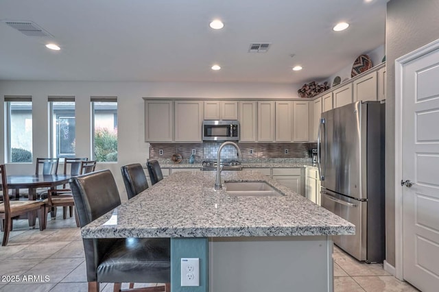 kitchen featuring sink, a kitchen bar, a kitchen island with sink, light stone counters, and stainless steel appliances