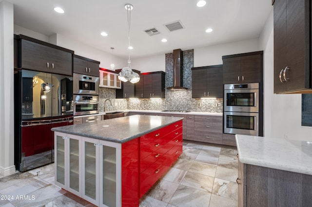 kitchen with black fridge, hanging light fixtures, a kitchen island, wall chimney range hood, and double oven