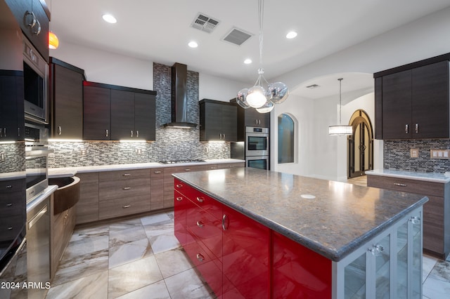 kitchen with gas cooktop, double oven, a kitchen island, decorative light fixtures, and wall chimney exhaust hood