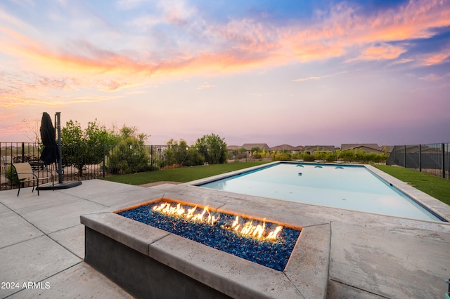 pool at dusk with an outdoor fire pit, a yard, and a patio area