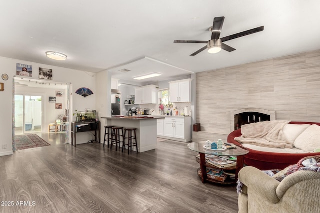 living room featuring dark wood-type flooring, visible vents, ceiling fan, and a tiled fireplace