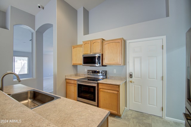 kitchen featuring light brown cabinetry, a towering ceiling, stainless steel appliances, and sink