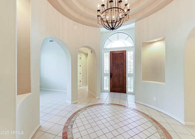 foyer featuring a raised ceiling, light tile patterned floors, baseboards, and a towering ceiling