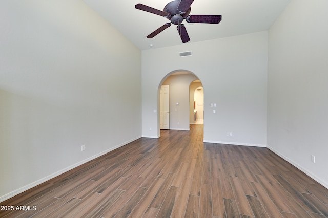 empty room featuring visible vents, arched walkways, baseboards, and wood finished floors