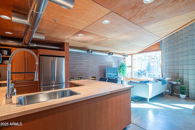 kitchen featuring open floor plan, butcher block counters, concrete flooring, wooden ceiling, and freestanding refrigerator