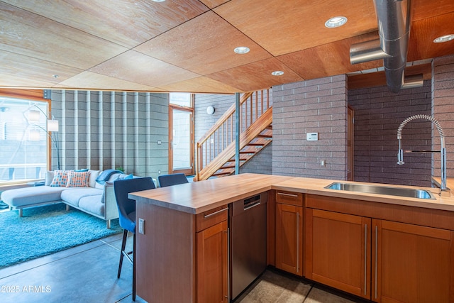 kitchen with brick wall, wood ceiling, stainless steel dishwasher, brown cabinetry, and a sink