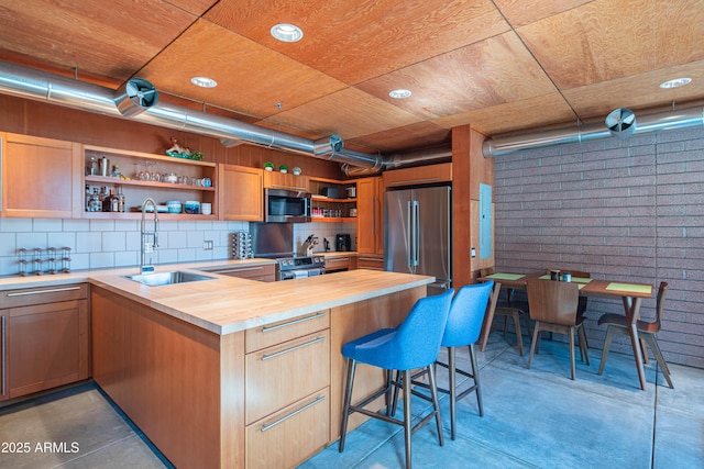 kitchen with tasteful backsplash, open shelves, butcher block counters, stainless steel appliances, and a sink