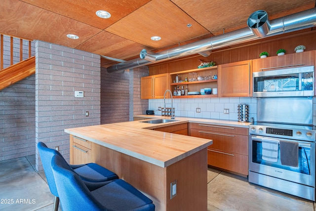 kitchen featuring brick wall, concrete floors, a sink, appliances with stainless steel finishes, and wood counters