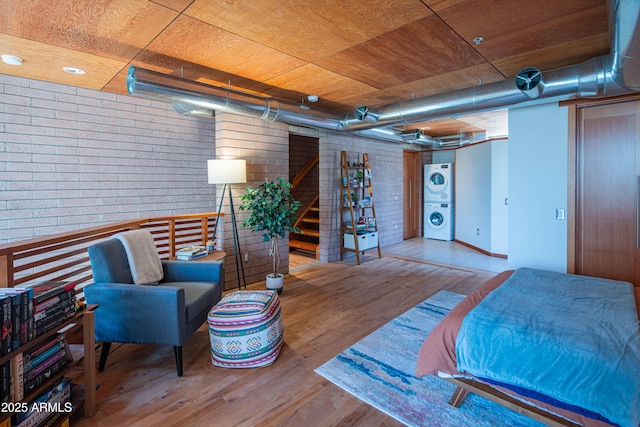 bedroom with stacked washer / drying machine, wood finished floors, and brick wall