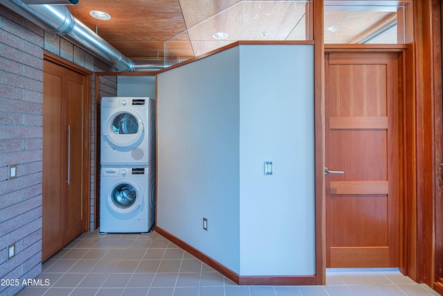 laundry room featuring light tile patterned floors, stacked washer / dryer, laundry area, and baseboards