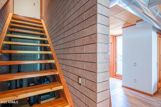 stairs featuring brick wall, an accent wall, baseboards, and wood finished floors