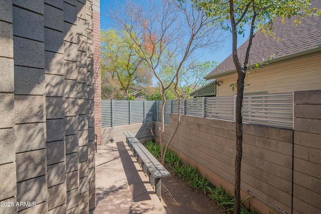 view of side of home featuring a fenced backyard and a shingled roof