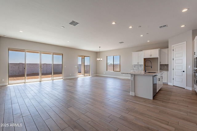 kitchen with sink, white cabinets, light wood-type flooring, backsplash, and a center island with sink