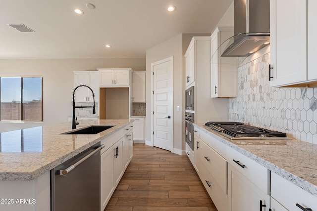 kitchen featuring sink, white cabinets, light stone countertops, wall chimney range hood, and appliances with stainless steel finishes