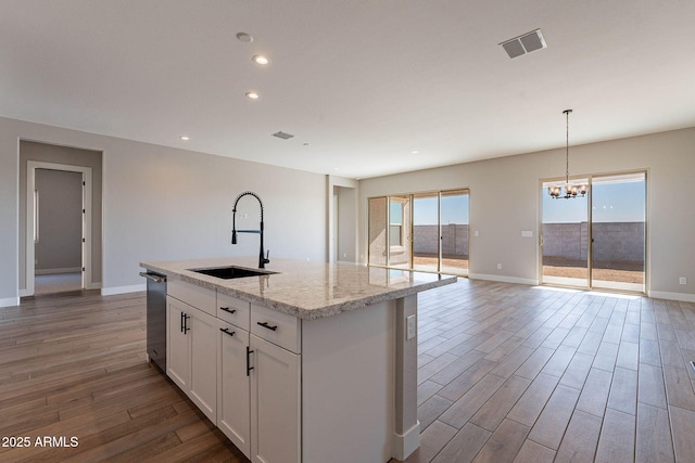 kitchen with white cabinets, an island with sink, light stone countertops, sink, and decorative light fixtures